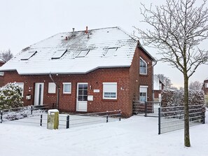 Une maison en briques rouges, avec un toit recouvert de neige et un portail en métal devant.