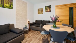 Ein modernes Wohnzimmer mit einer Couch, einem Couchtisch und einem Esstisch mit Stühlen. An den Wänden sind Dekorationen und ein Holztür.