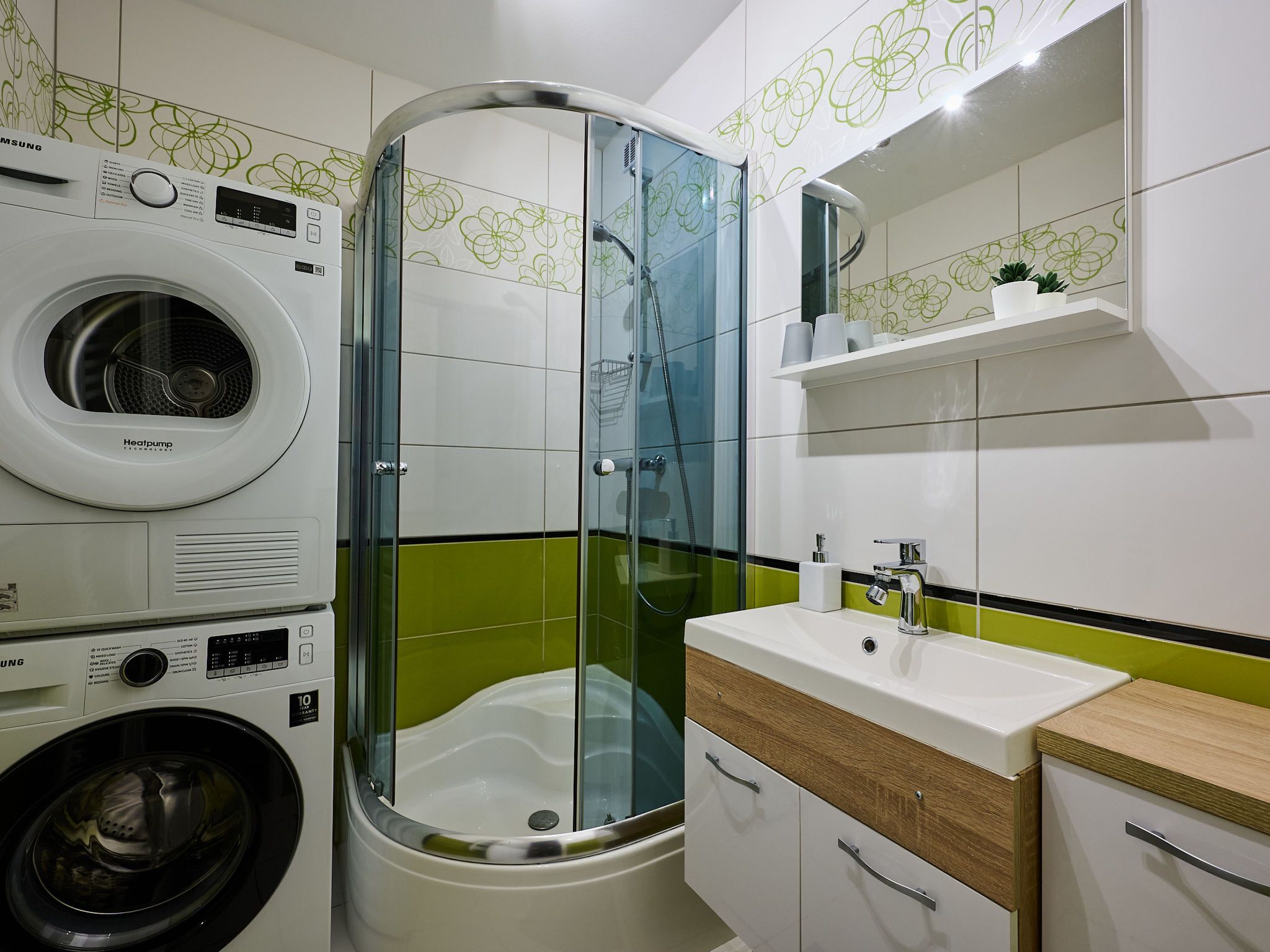 Een moderne badkamer met een glazen douchecabine, een ingebouwde wasmachine en een wastafelmeubel met wastafel en spiegel.