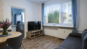 Ein modernes Wohnzimmer mit Flachbildfernseher, einem Esstisch mit Stühlen, einer Couch und einem Fenster mit Vorhängen.