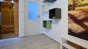Ein Flur mit einer Holztür, einer weißen Wand mit drei schwarzen Regalen und einem großflächigen Waldgemälde.