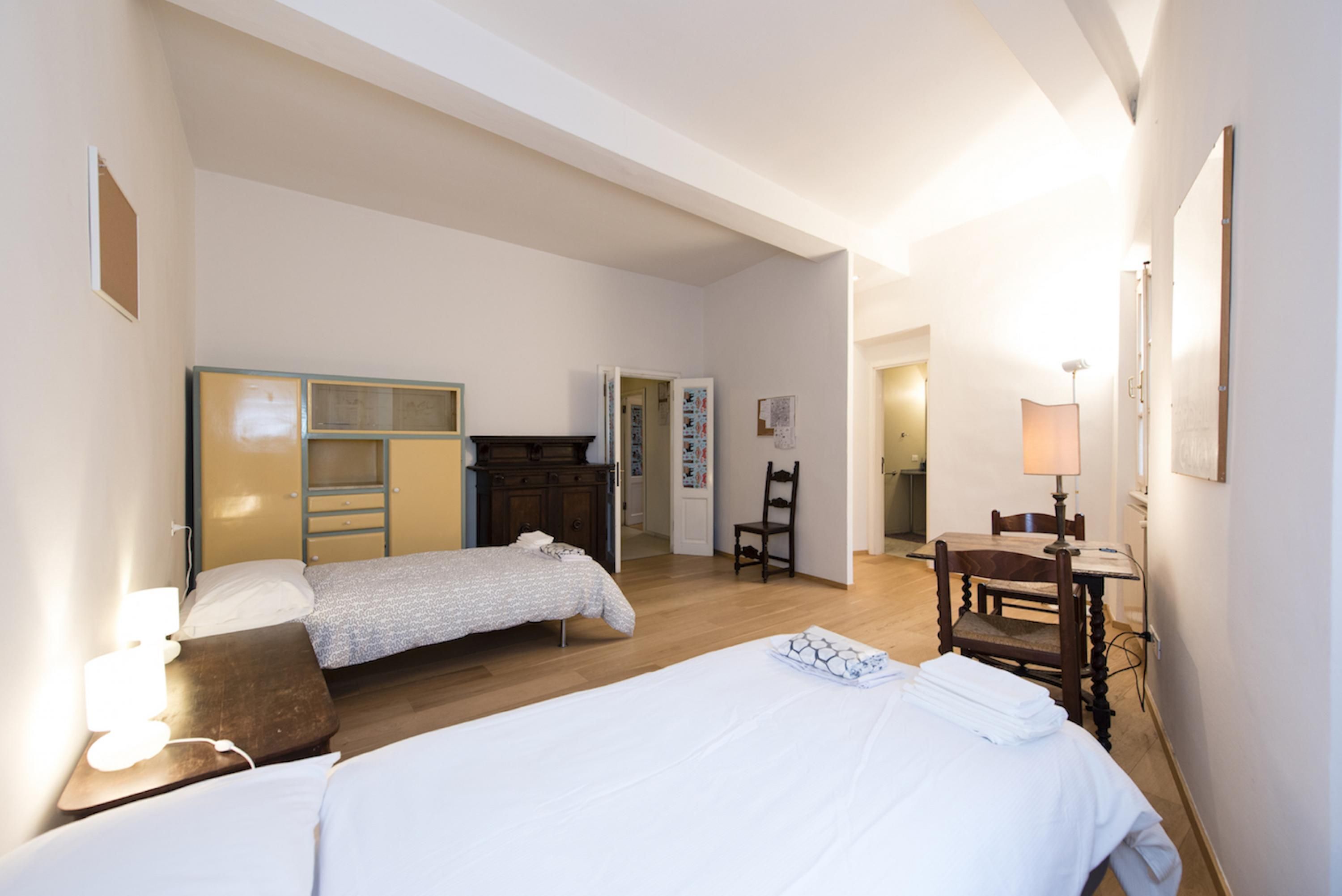 A room with two beds, a wooden dresser, a chair, and a desk with a lamp.
