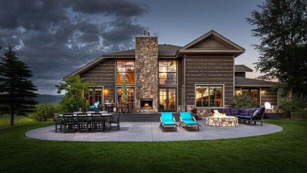 A modern house with a stone fireplace, outdoor seating, and a view of the mountains. - Month long Rental- Teton Springs Home 4 Bedroom (Victor)