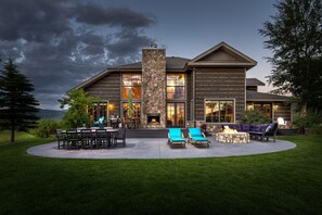 A modern house with a stone fireplace, outdoor seating, and a view of the mountains. - Month long Rental- Teton Springs Home 4 Bedroom (Victor)