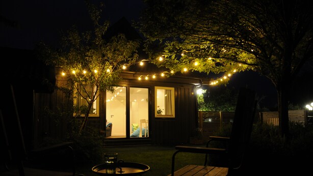 A cozy outdoor patio with string lights, a wooden table, and chairs.