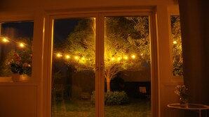 A glass door entrance with a view of a garden at night, illuminated by string lights.