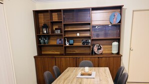 Un comedor con una mesa y sillas de madera, una estantería con varios objetos, y una puerta al fondo.