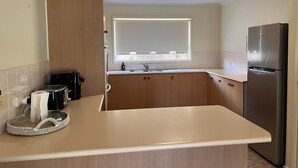 Una cocina con armarios de madera, un refrigerador de acero inoxidable, una ventana con persianas y una encimera con una cesta y una botella.