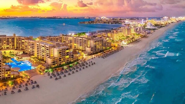 Een hotel aan het strand met meerdere gebouwen, een zwembad en een strand met parasols.