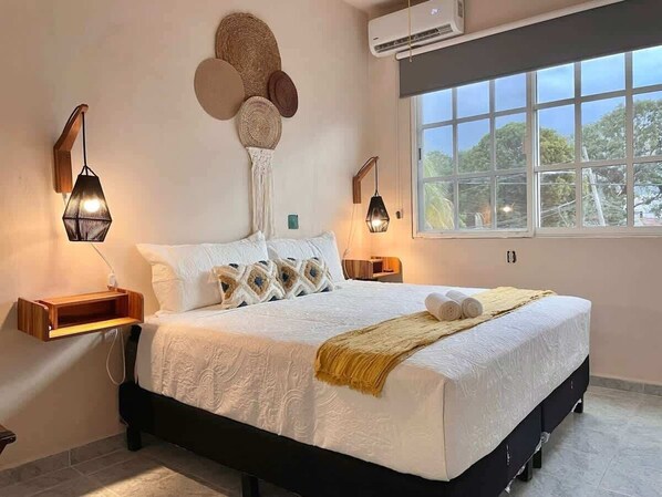 A bedroom with a bed, bedside lamps, a wall-mounted air conditioner, and a window with a view.