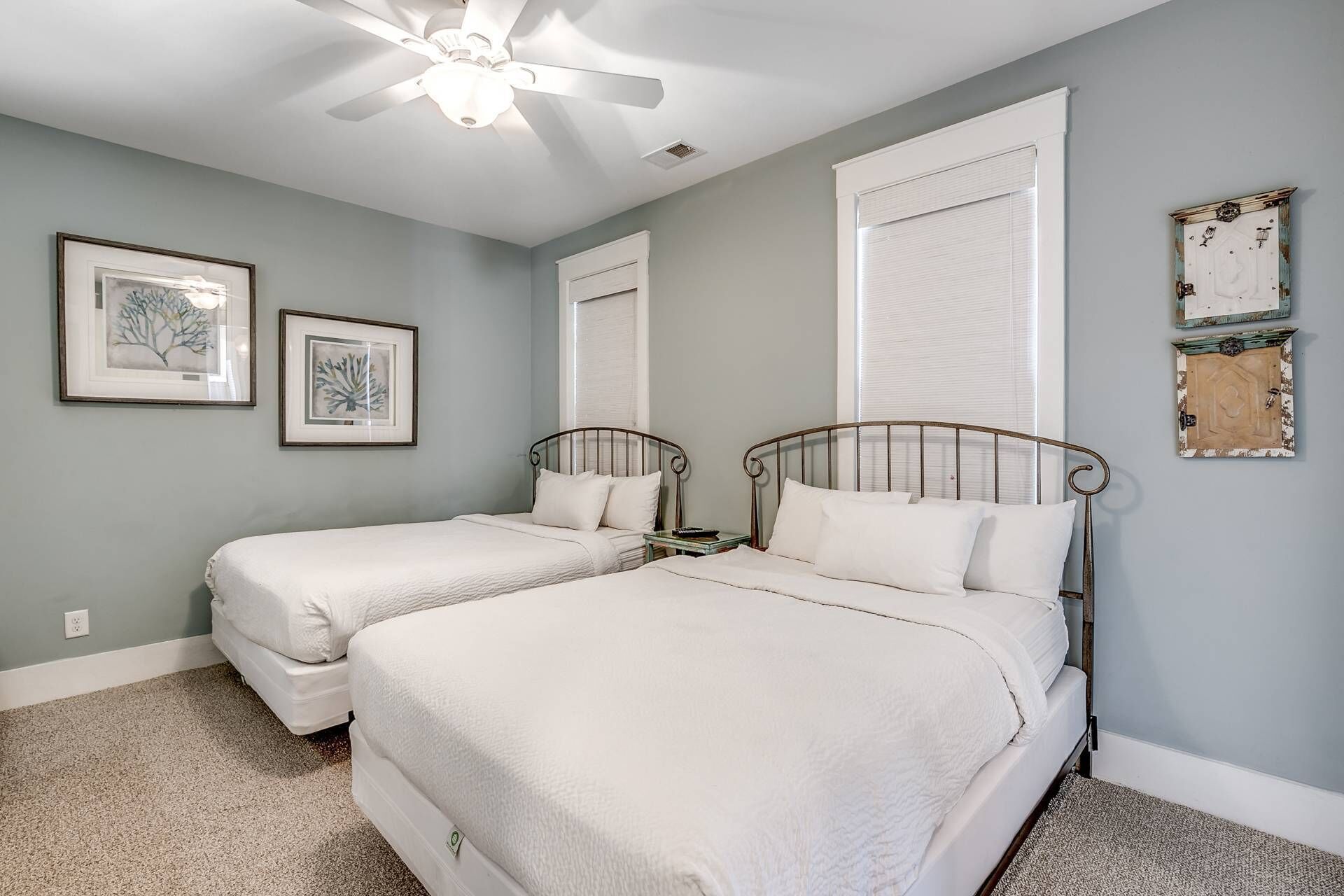 A bedroom with two beds, a ceiling fan, and framed artwork on the walls.