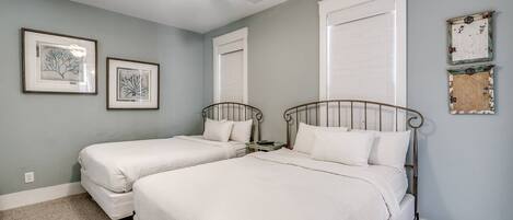 A bedroom with two beds, a ceiling fan, and framed artwork on the walls.