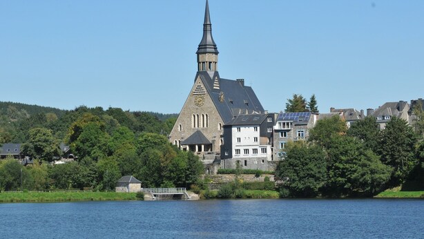 Een kerk met een hoge spits, een klok en een zonnepaneel op het dak.