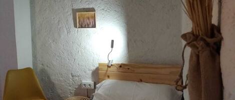 A small, rustic bedroom with a single bed, a wooden headboard, a yellow chair, and a wall-mounted lamp.
