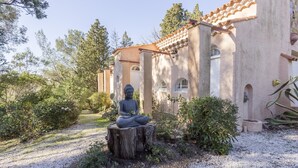 Une statue représentant une figure assise, placée dans un jardin, avec un bâtiment en arrière-plan.