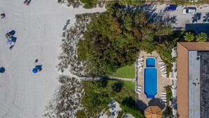 En vy från ovan av en fastighet vid stranden, med en swimmingpool, solstolar och en täckt uteplats.