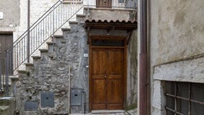 A stone building with a wooden double door, a metal staircase, and a metal gate.