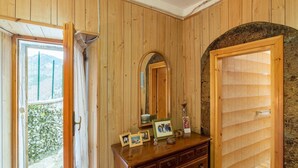 A wooden-paneled room with a stone arch doorway, a wooden dresser with framed photos, and a window overlooking a garden.
