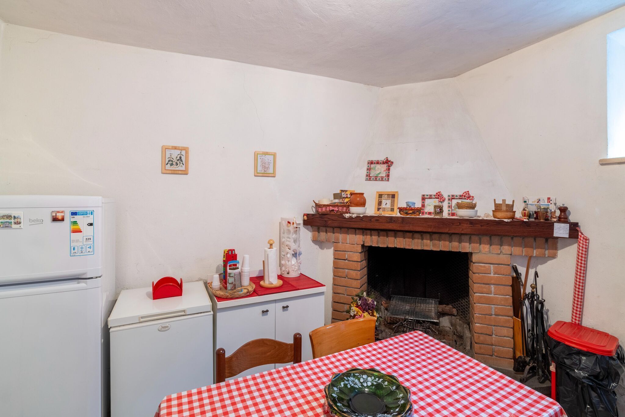 A compact kitchen with a brick fireplace, a refrigerator, and a table set with a checkered tablecloth.