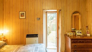 A room with wooden walls, a bed, a dresser, and a door leading to an outdoor area.