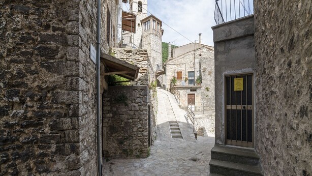 A narrow stone street with a staircase leading to a building with a barred window.