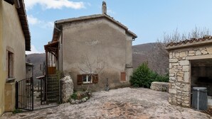 A rustic courtyard with stone flooring, a gate, and a building with wooden shutters.