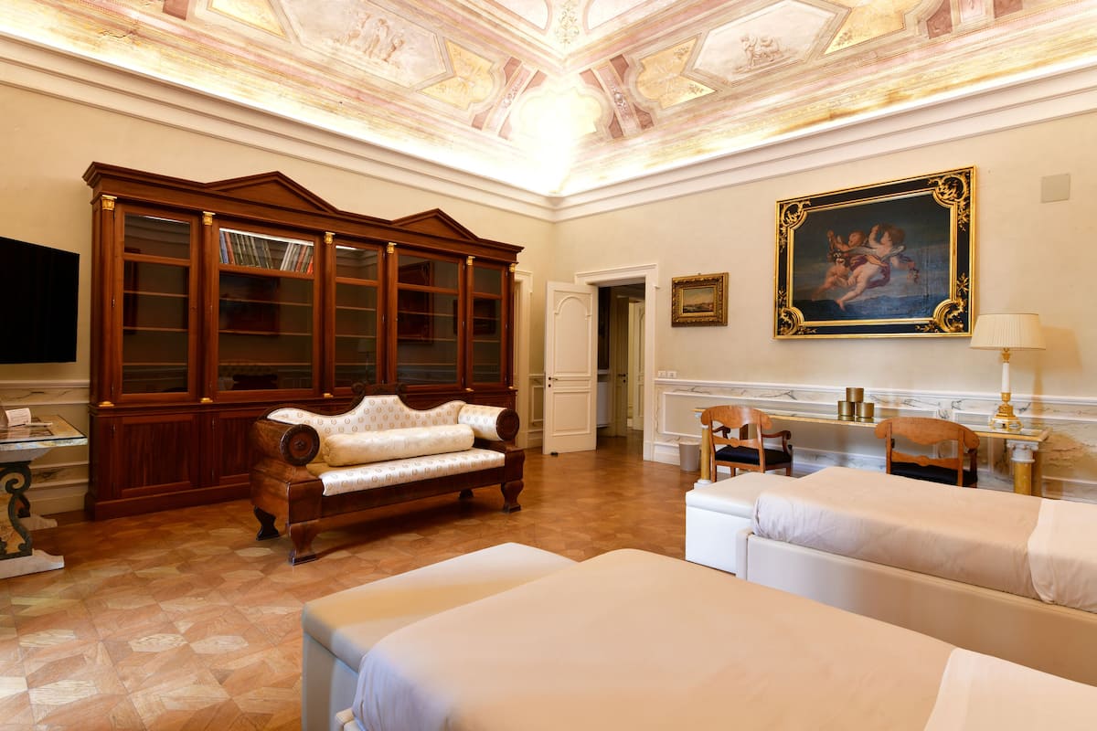 A spacious room with a large wooden cabinet, a sofa, two beds, and a painting on the wall.