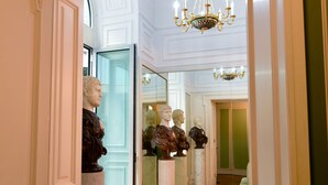 Un couloir orné de colonnes en marbre, d’un lustre et d’un mur recouvert de miroirs qui reflètent la pièce.