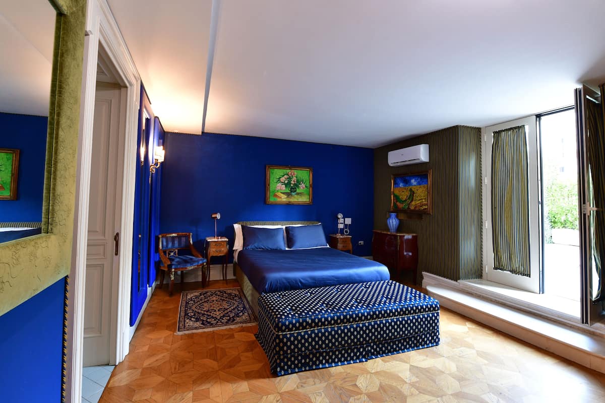 A bedroom with a large bed, a window with curtains, a nightstand, and a chair.