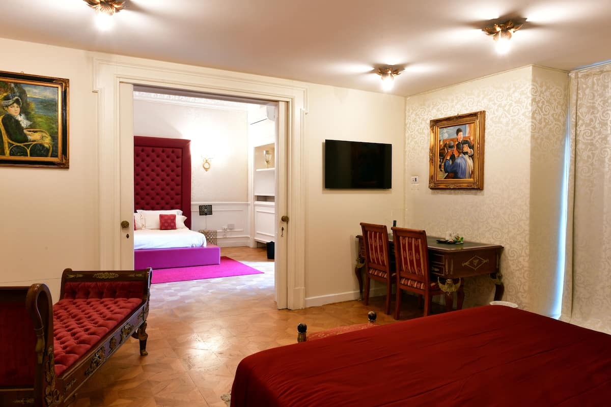 A hotel room with a large bed, a red armchair, a wooden desk, and a television.