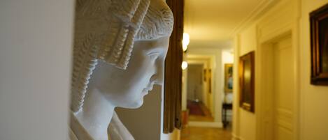 A hallway with a classical sculpture on the wall, a red carpet, and framed artwork on the walls.