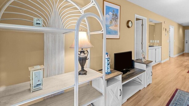 A room with a curved white metal partition, a wooden desk with a lamp, a television, and a framed picture on the wall.