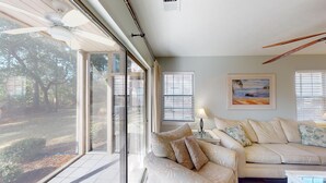 A spacious living room with a large window, a ceiling fan, and a painting on the wall. - Fairway Escape Modern 3BR with Scenic Views (Pawleys Island)