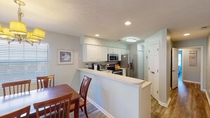 A modern kitchen with white cabinets, stainless steel appliances, and a wooden dining table with chairs. - Fairway Escape Modern 3BR with Scenic Views (Pawleys Island)