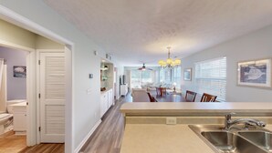 A spacious kitchen with a large island, a dining area with a chandelier, and a view of the outdoors through large windows. - Fairway Escape Modern 3BR with Scenic Views (Pawleys Island)