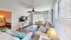 A spacious living room with a large sofa, a television, and a ceiling fan. - Fairway Escape Modern 3BR with Scenic Views (Pawleys Island)