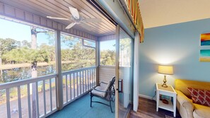 Eine überdachte Veranda mit Deckenventilator, einem Sessel, einem kleinen Tisch mit Lampe und Blick auf Bäume und Wasser.