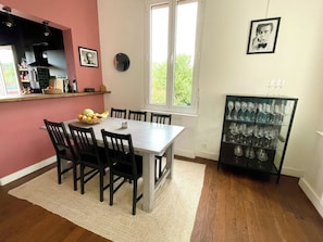 A dining area with a table and chairs, a fruit bowl, a wine rack, and a window with a view.