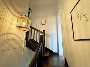 Een trap met een houten leuning, een aan de muur hangend schilderij en een hanglamp.