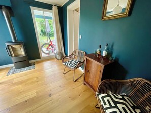 A room with a wood-burning stove, two wicker chairs, a wooden cabinet, and a view through a glass door.