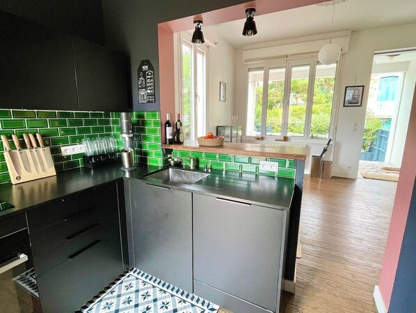 A modern kitchen with green tiles, stainless steel appliances, and a view of a balcony.