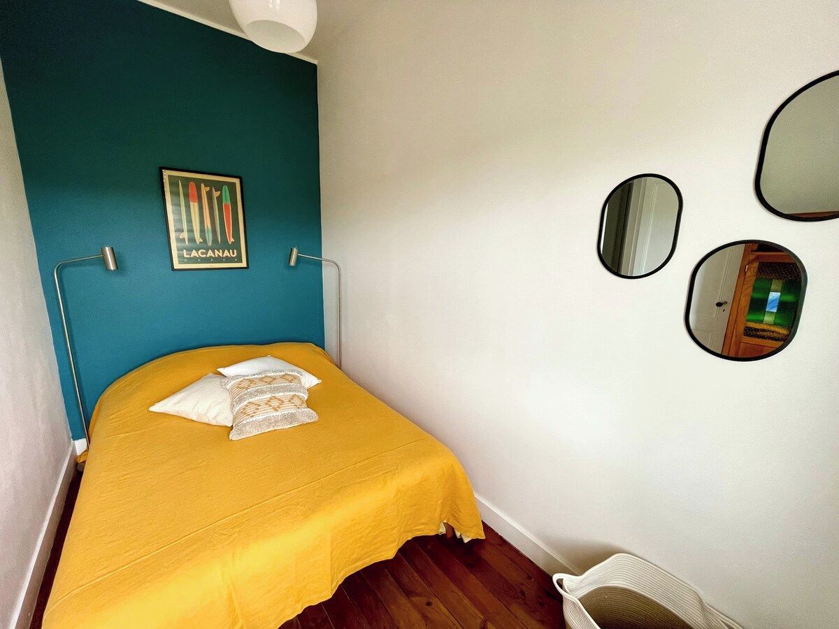 A small bedroom with a bed, a blue wall, a framed picture, and a mirror.