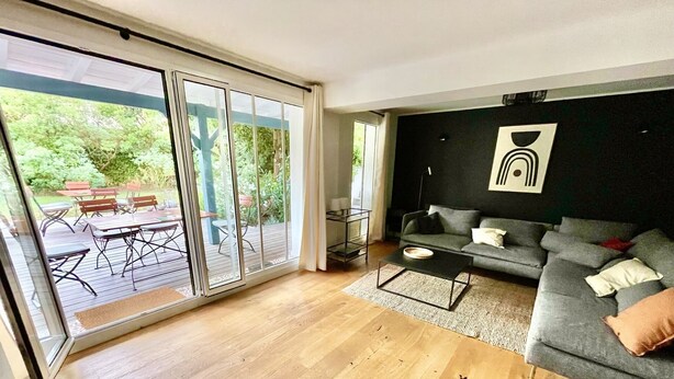 Ein modernes Wohnzimmer mit grauem Sofa, einem Couchtisch und einer Schiebetür zu einer Terrasse mit Holzmöbeln.