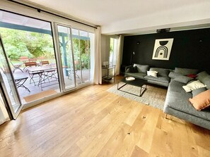 Ett modernt vardagsrum med en grå soffa, ett soffbord och en skjutdörr i glas som leder ut till en uteplats med trädgårdsmöbler.