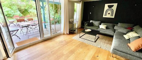 Een moderne woonkamer met een grijze bank, houten vloeren en een schuifdeur naar een terras.