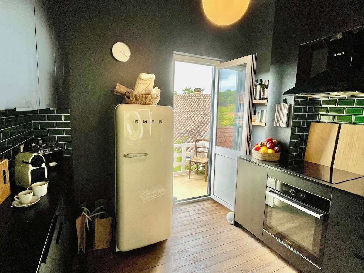 Eine Küche mit Kühlschrank, Backofen und einem Fenster, das zu einem Außenbereich führt.