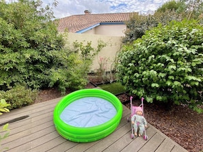 An outdoor inflatable pool on a wooden deck with a child in a stroller nearby.