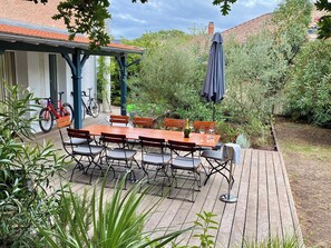 Een terras buiten met een houten tafel en stoelen, omgeven door groen en een fiets.