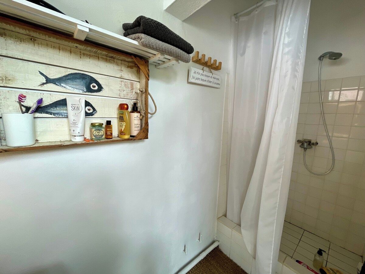 Une salle de bain avec une douche, une étagère contenant des articles de toilette et un panneau fixé au mur.
