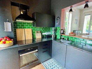 A modern kitchen with a black stove, green backsplash, and a wooden countertop.